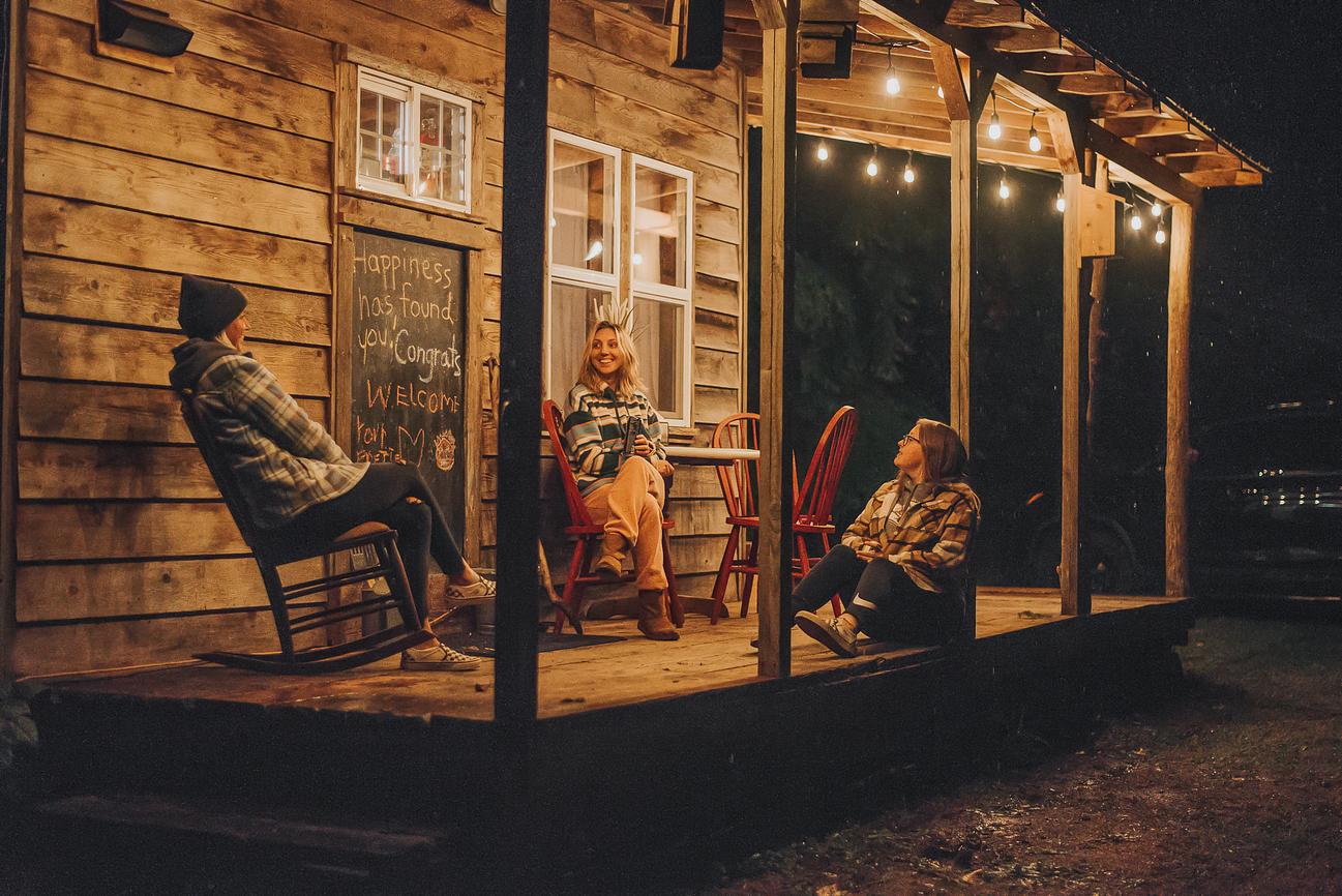 Photo of three ladies on the porch at one of the Happy Hotelier cabins at night. Image for Merry & Bright Promotion.